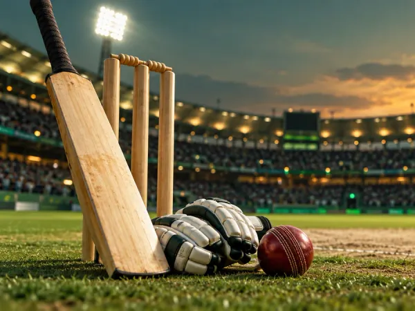 cloudbet cricket bat, red ball, batting gloves and stumps beside a floodlit pitch